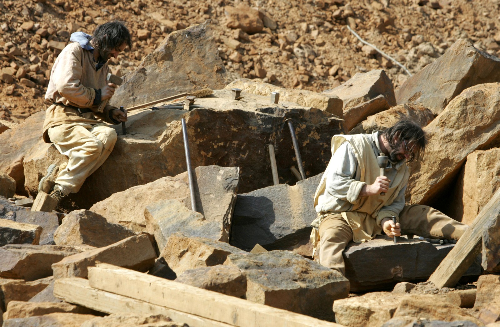 Stonecutters in medieval-style clothing work at a construction site.
