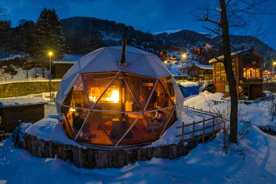 An illuminated dome house covered with snow, at night, in an alpine community