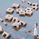 A woman stands on a cube-shaped concrete block, among many such blocks piled haphazardly in shallow water.