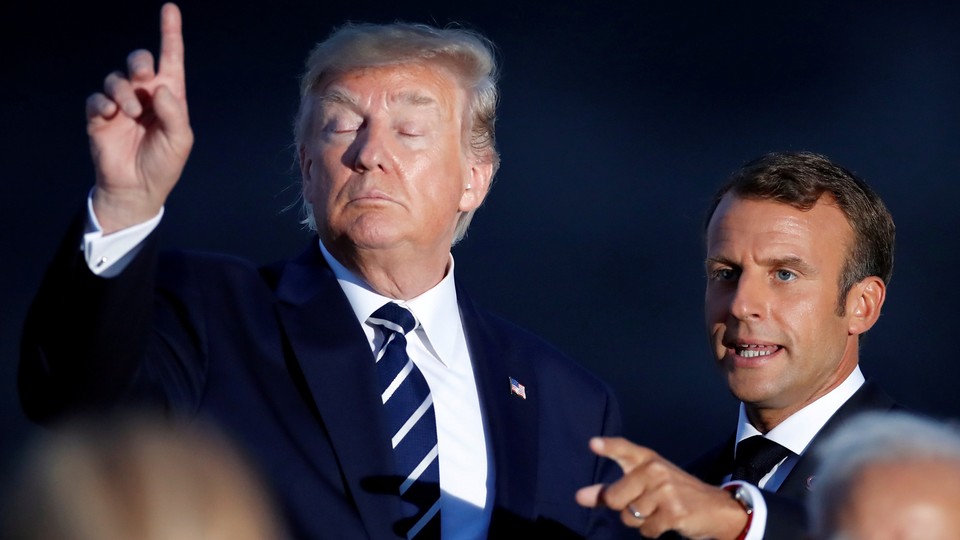President Trump raises a finger while French president Emanuel Macron points to a reporter in the distance.
