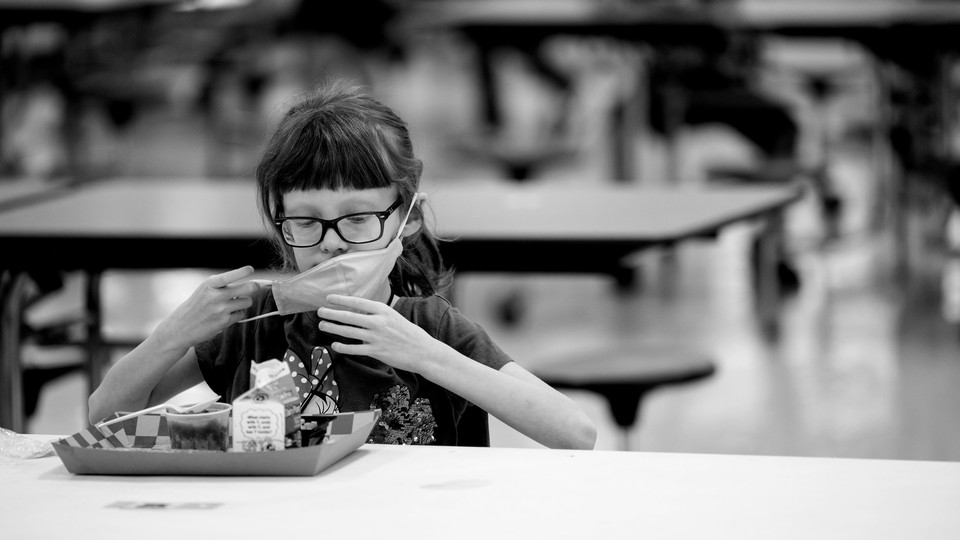 A girl taking off her mask to eat school lunch alone