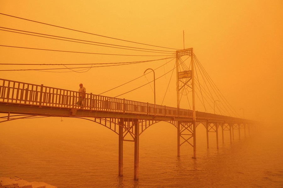 A man walks along a pedestrian bridge as dust in the air obscures the bridge and makes the sky orange.