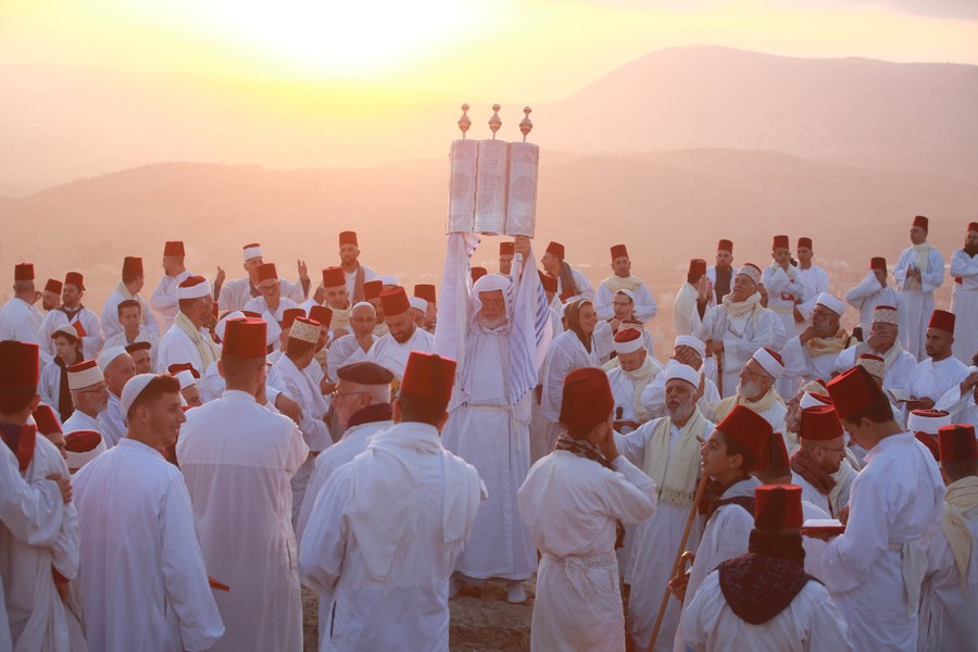 A group of people wearing traditional white clothing gather together on a hilltop.