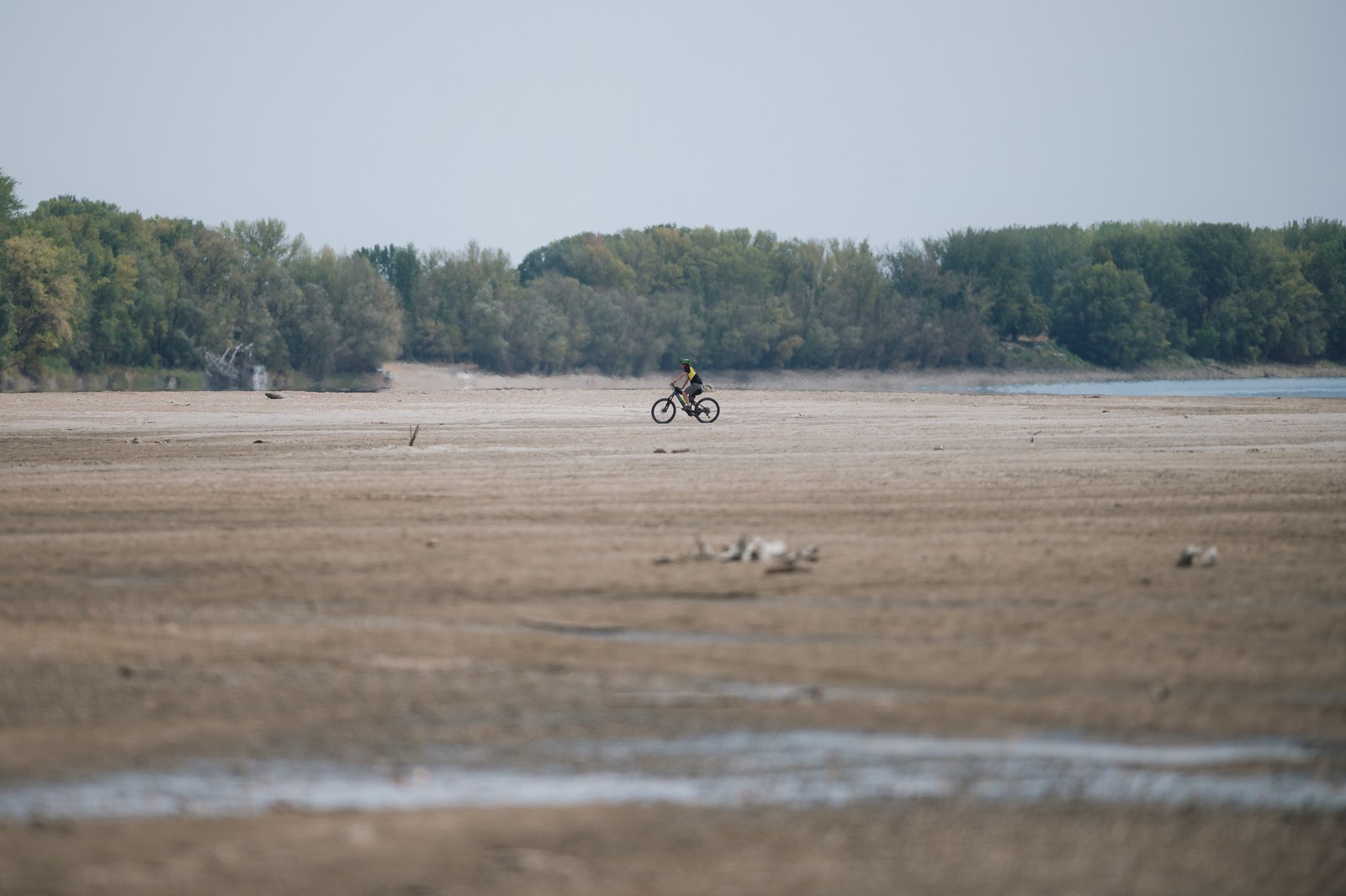 A cyclist rides across a dry riverbed.