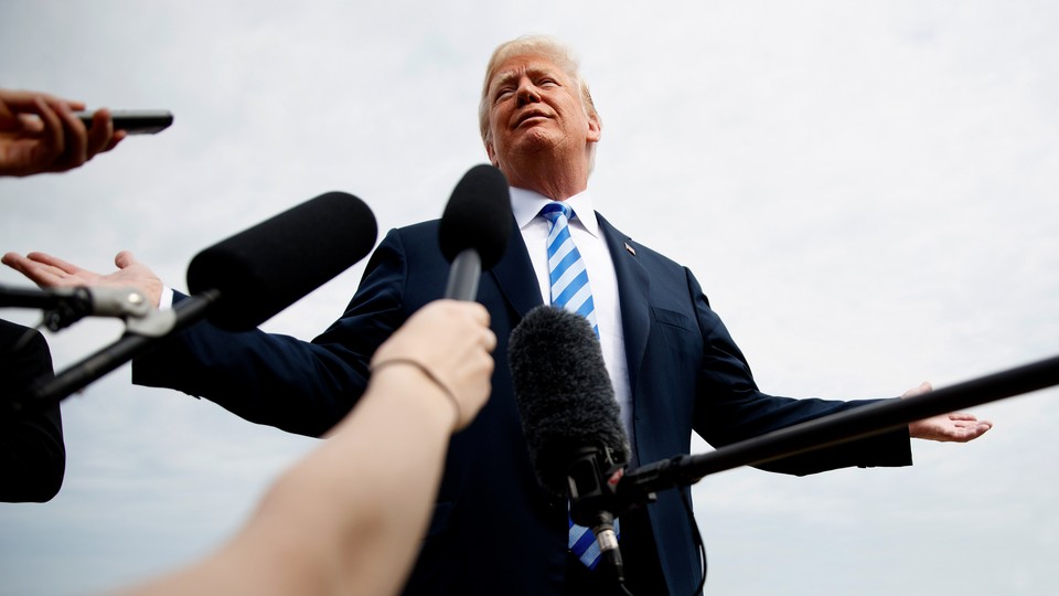 Donald Trump stands, arms outstretched, behind a row of hands holding microphones.