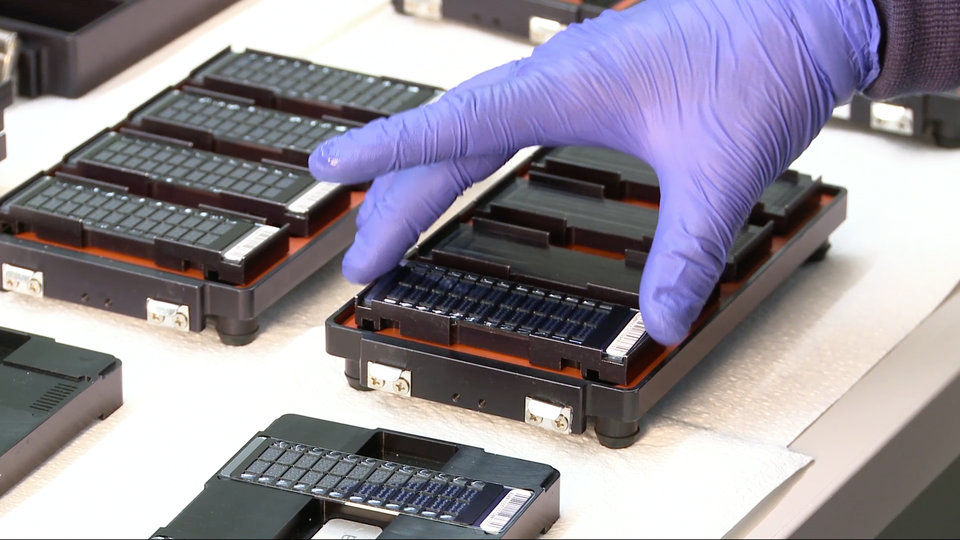 A gloved hand manipulates an electronic chip.