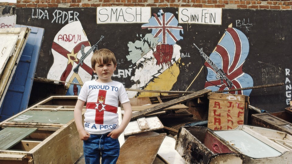 A boy stands in front of unionist murals in West Belfast.