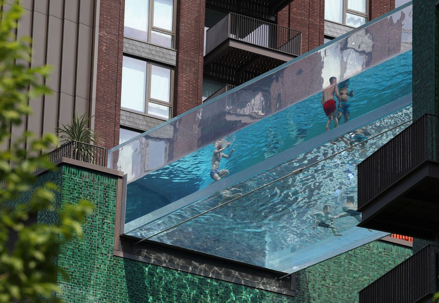 People relax in a clear swimming pool suspended between two buildings.