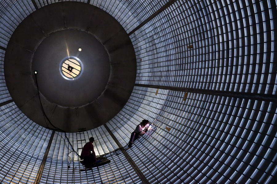 Two people work inside an enormous cylindrical tank, welding metal on the side.