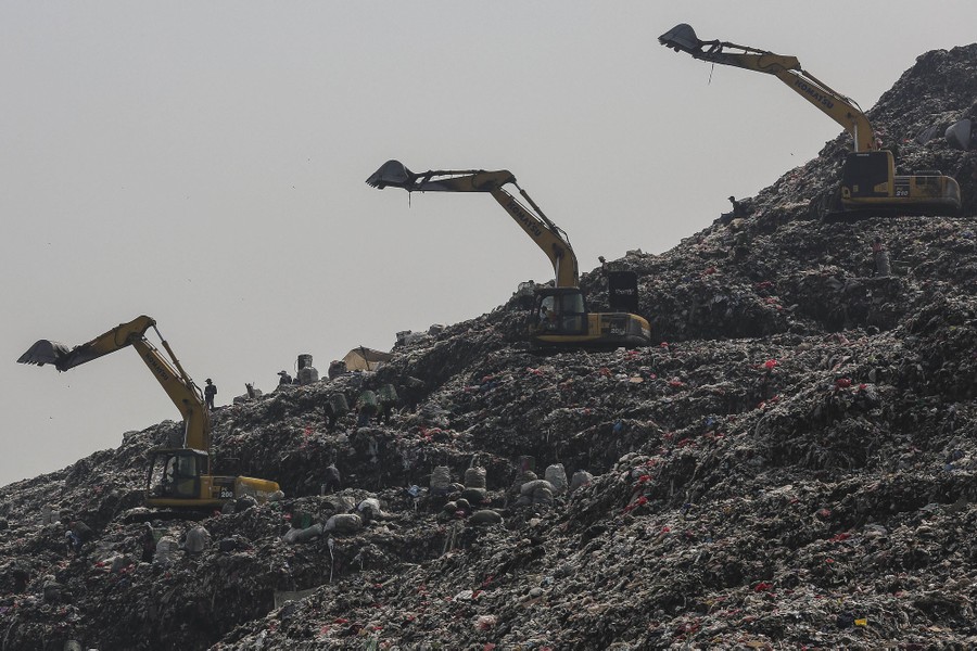 Several excavators sit on top of a small mountain of garbage.