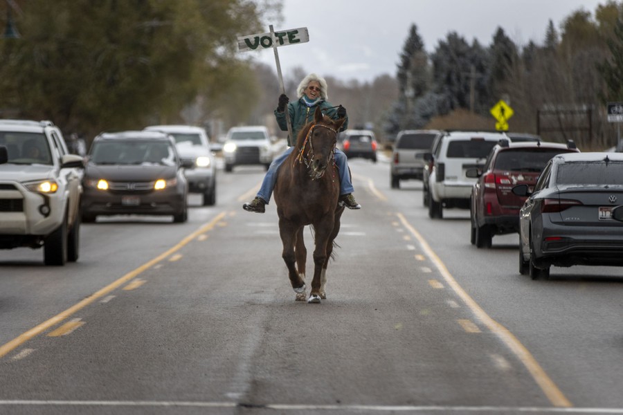 A person rides a horse down the median of a busy street, carrying a sign that reads "Vote."