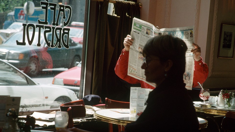 A man in a café holds up a newspaper to read it.