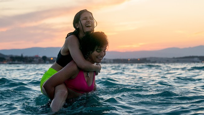 One girl carries another on her back as they swim, laughing, in "The Swimmers"