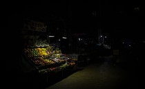 A fruit stand is lit by two small lamps on a very dark street.