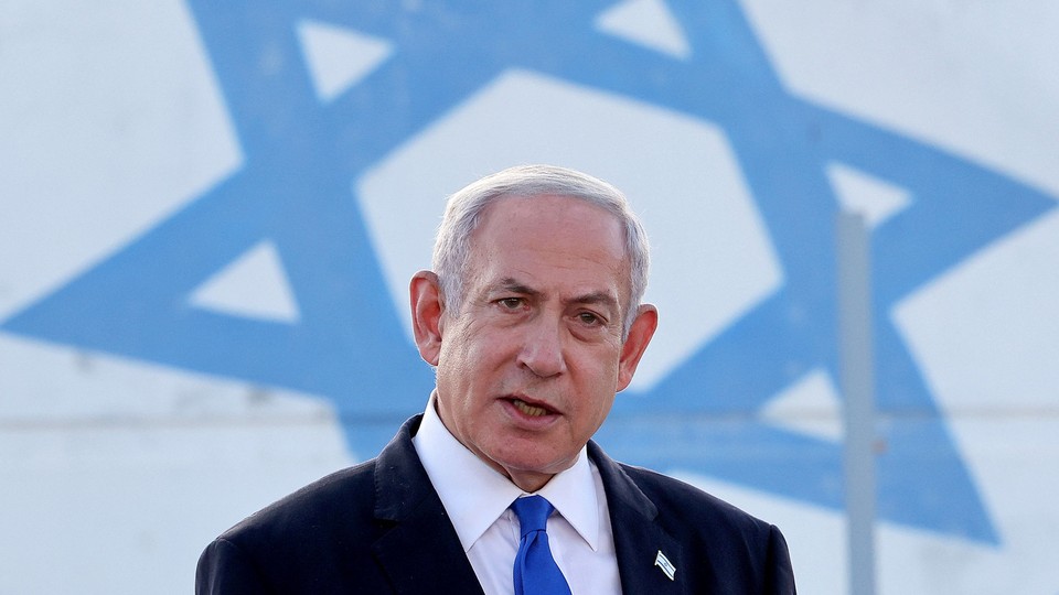 A photograph of Benjamin Netanyahu speaking in front of a large Israeli flag