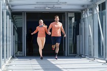 A still from the TV show The Amazing Race featuring a couple team in light orange athletic clothing running through an airport terminal