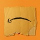 A torn piece of an Amazon box, the logo upside down, rests against an orange background.