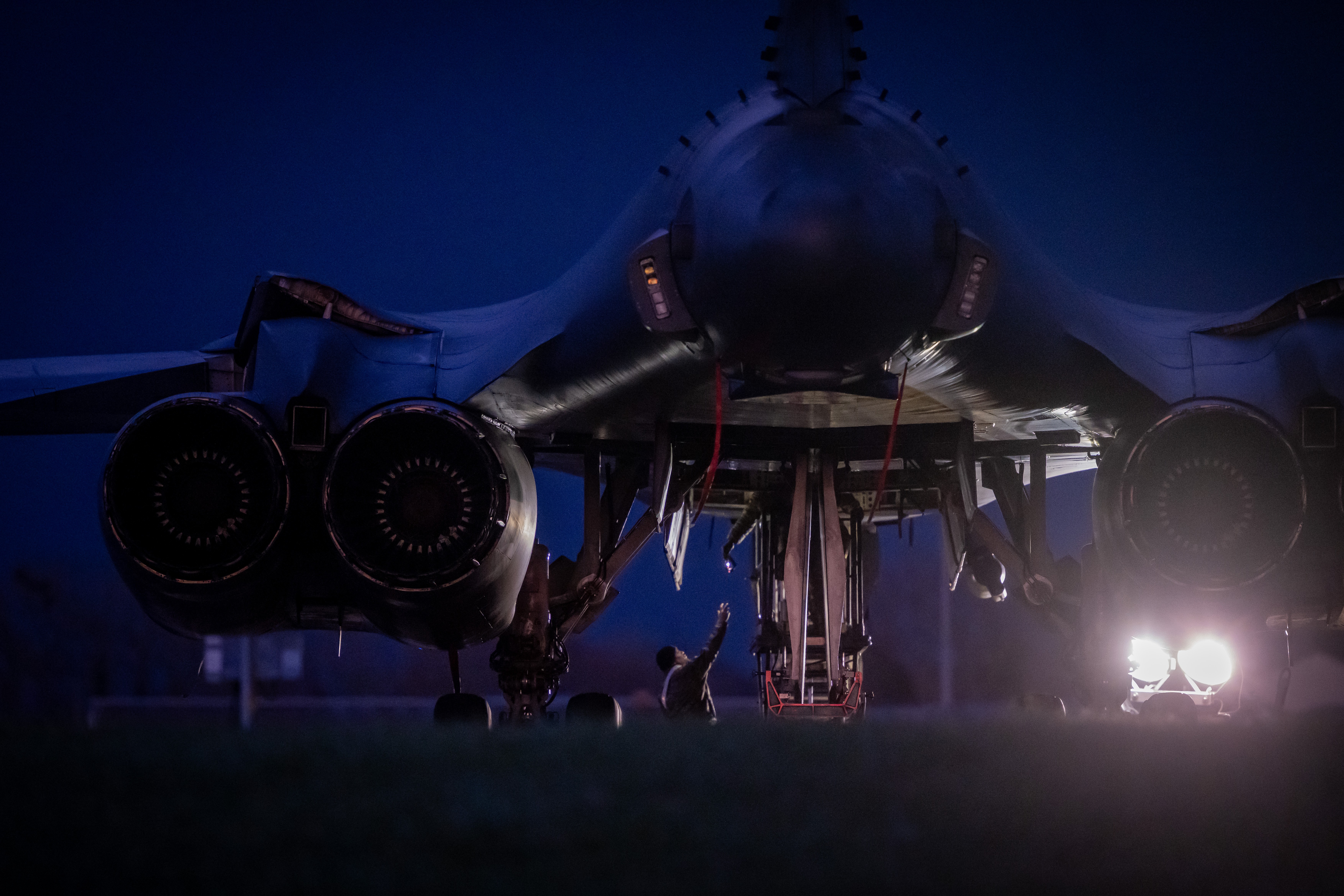 People work beneath a bomber aircraft, reloading munitions, seen at night.