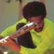 André 3000 crouching in a neon yellow-green shirt holding a flute