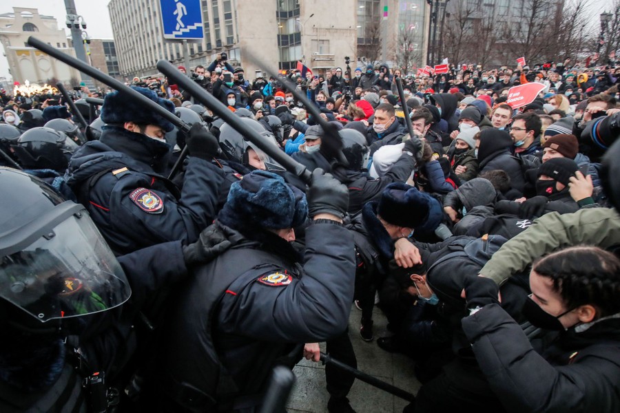 Riot police beat protesters in a crowded scene.