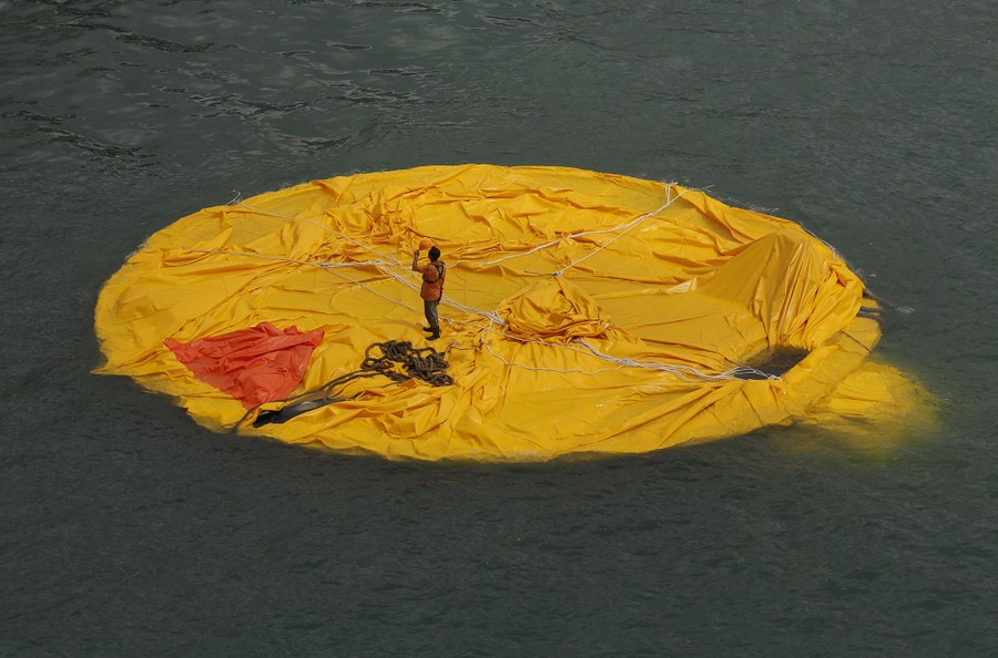 A person stands on a floating circle of yellow material that is a deflated giant rubber duck