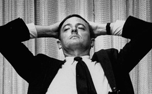 William F. Buckley sits with his hands placed behind his head.