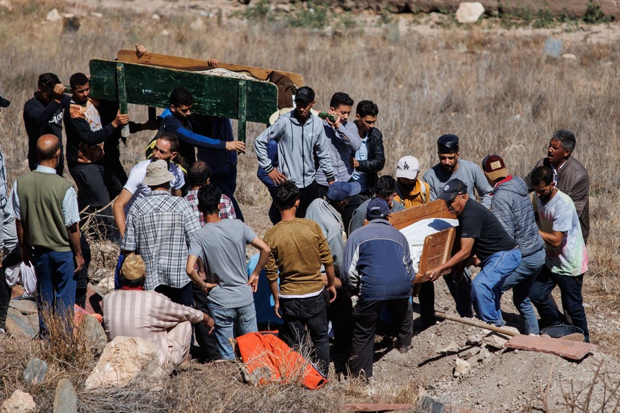 A group of people carries two bodies into a hillside cemetery.