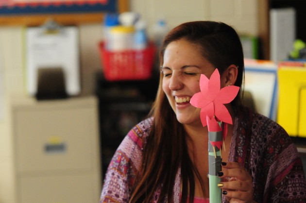A student smiles while holding up a paper flower.