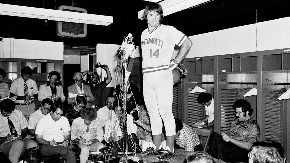 A black-and-white photo of Pete Rose addressing reporters in a locker room