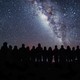 A group of people standing silhouetted against a star-filled sky