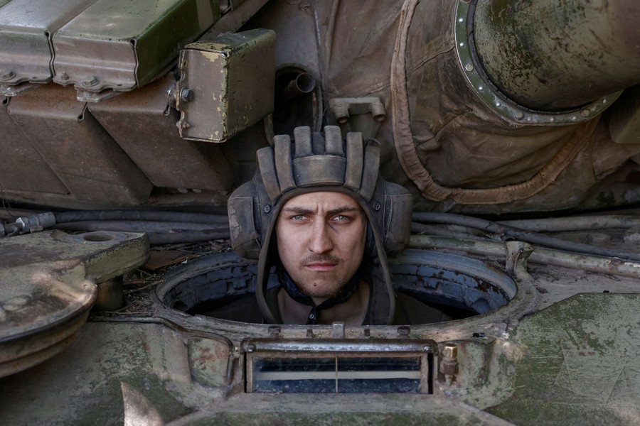 A soldier pokes his head out of an opening in the tank he is seated in.