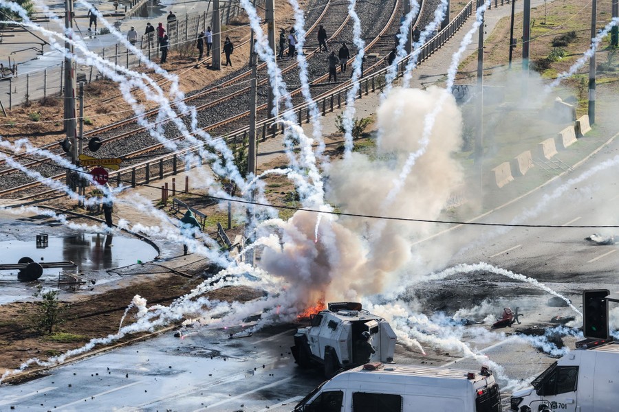 A police vehicle fires canisters of tear gas, leaving multiple streamers in the air.