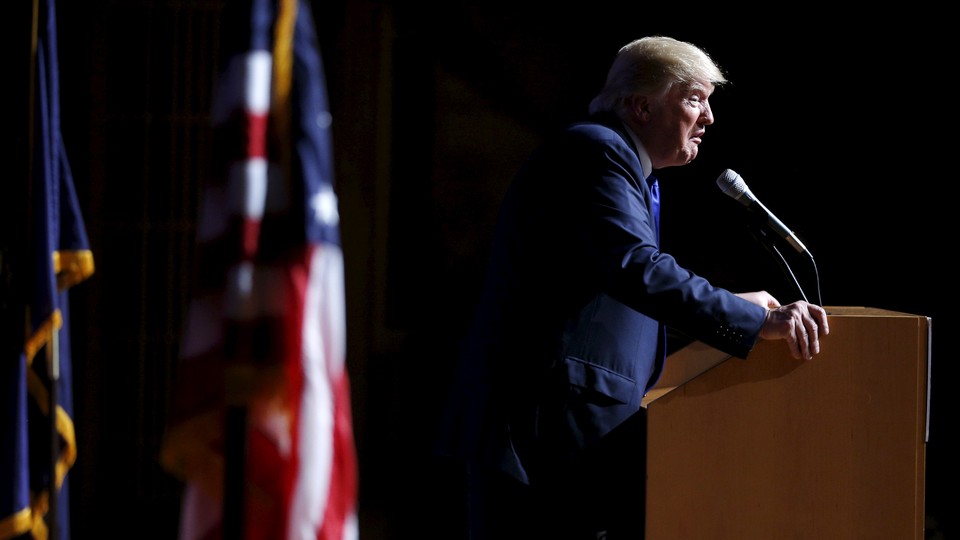 Donald Trump stands in front of a podium and an American flag.