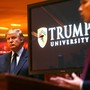 Donald Trump stands next to a screen that reads "Trump University."