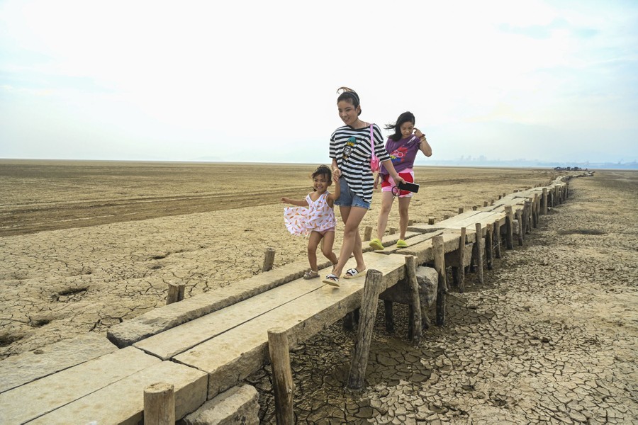 Three people walk on an old raised-platform bridge about thee feet above parched ground.
