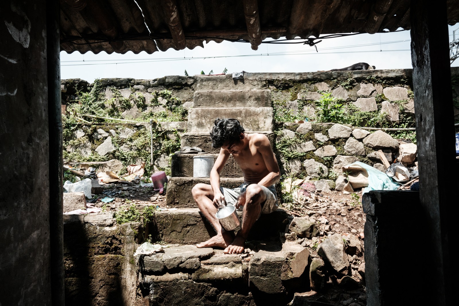 A man sits on concrete steps, mixing silver paint in a small bucket.