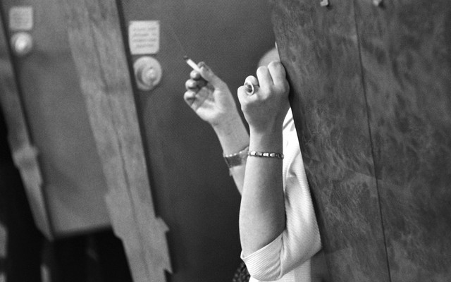Woman smoking cigarette behind a wall