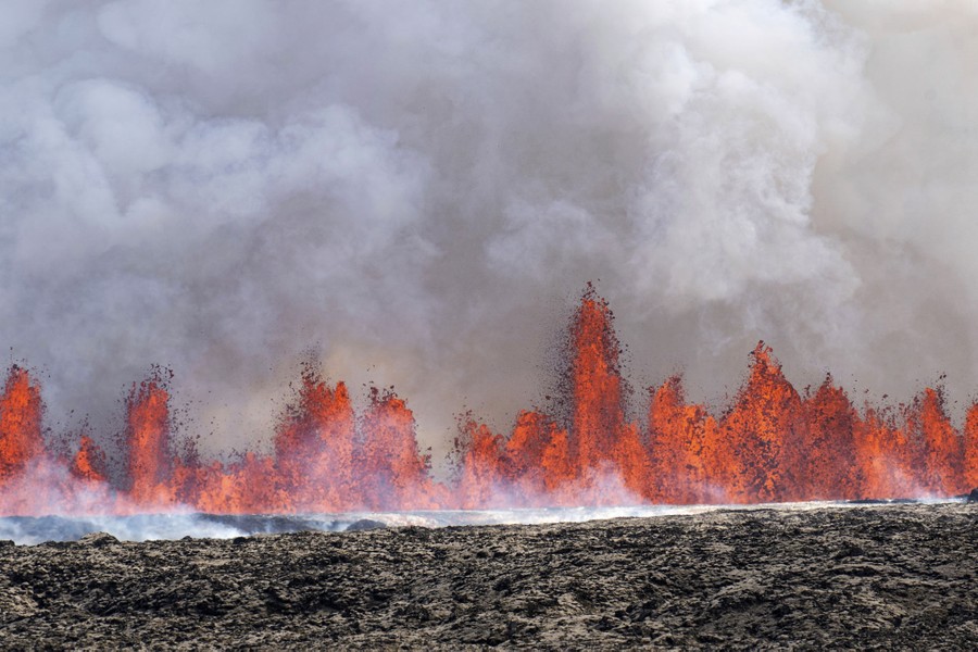 Many spouts of lava erupt along a fissure, creating a sort of wall of lava in the distance.