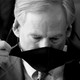 A black and white photo of Greg Abbott taking a mask off.