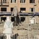 A woman in white stands before a shelled building