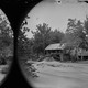 A black-and-white photograph of a house with a stream running near it, surrounded by trees and water