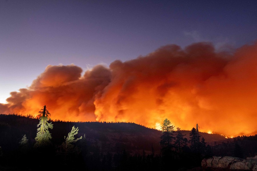 Rising plumes of smoke are lit by burning fires below, seen on a distant hillside.