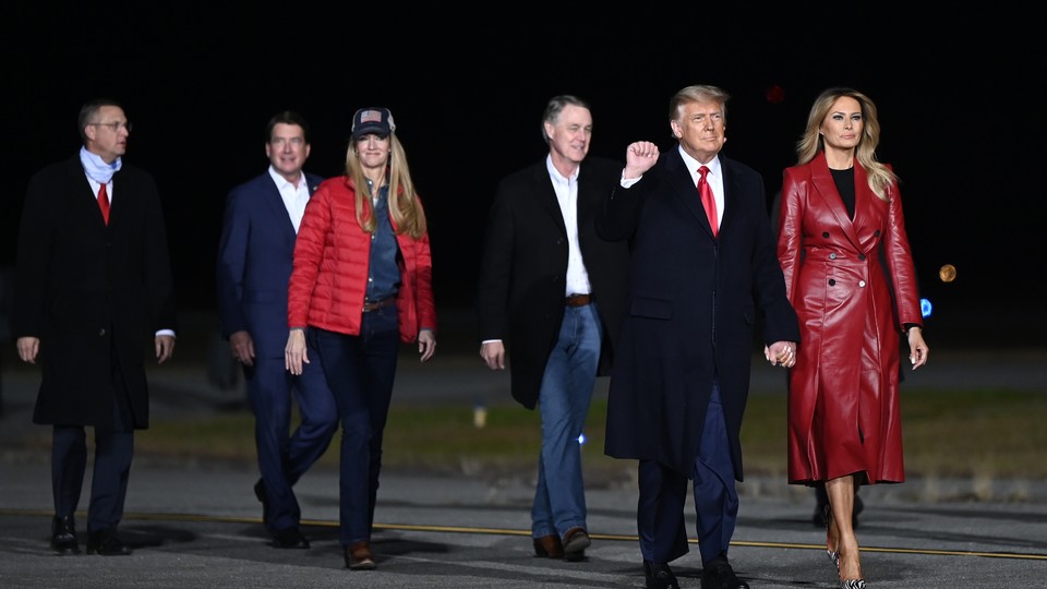 Donald Trump, Melania Trump, and the two Republican Senate candidates in Georgia walk with two others along an apparent tarmac. President Trump has his right fist raised.