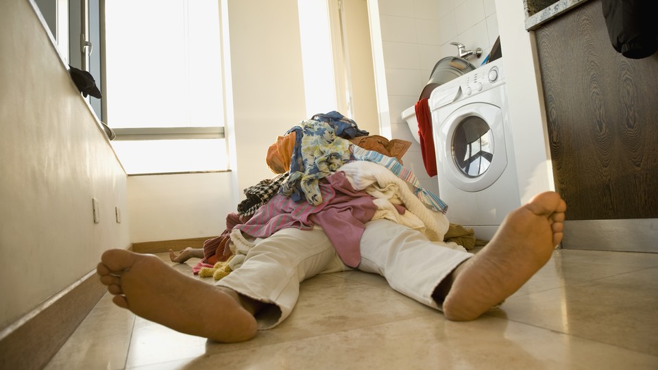 Someone laying on the ground in front of laundry machine with clothes on their lap