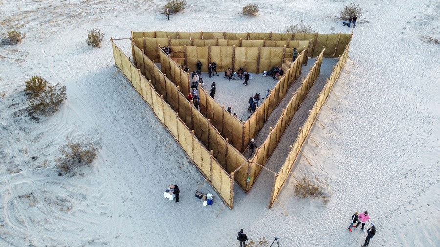 Visitors walk around a triangle-shaped group of fences in the desert.