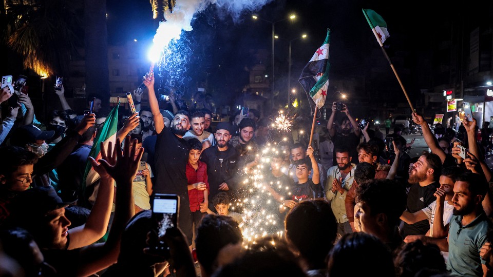 Syrians in a crowd light sparklers and wave flags on the street.
