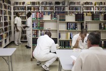 Men dressed in all white sit in a fluorescent room with bookshelves 