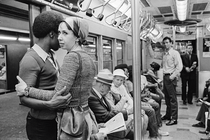 Black-and-white photograph of a couple holding each other on a crowded subway car