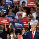 Donald Trump raises a fist, a crowd of supporters holding "save America!" signs stand behind him.