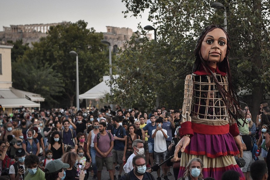 A crowd gathers around a tall puppet of a girl.